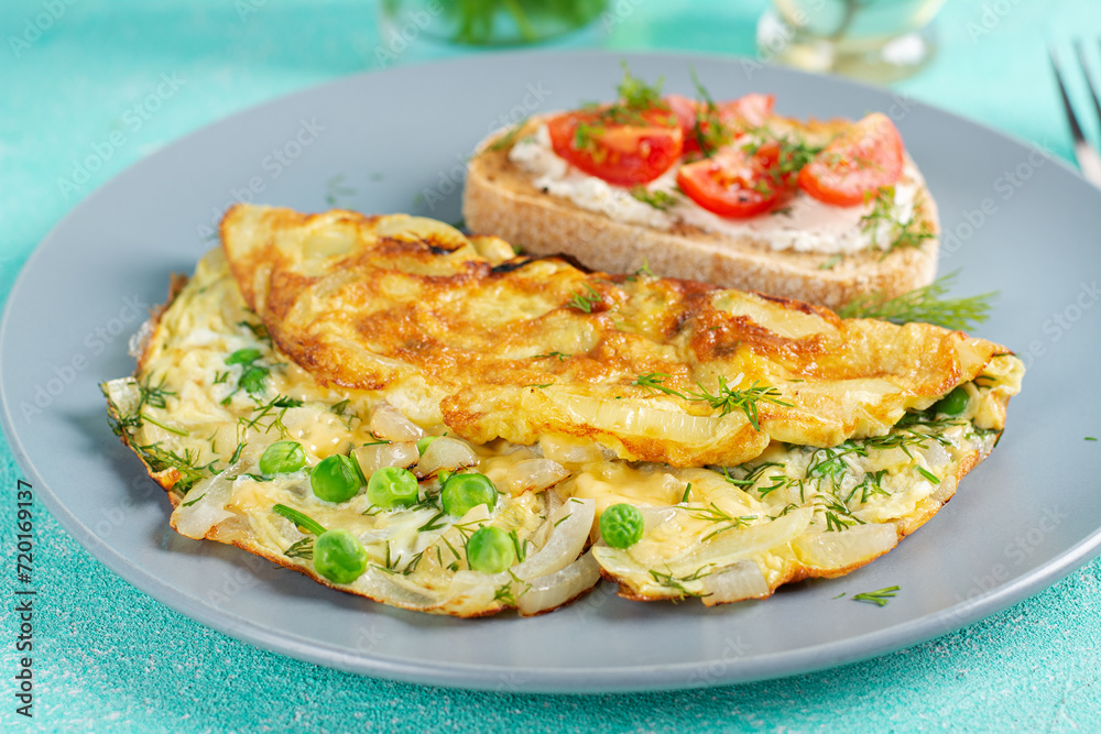 Omelette with green peas, onions and toast cream cheese, tomatoes on blue plate. Frittata - italian omelet.