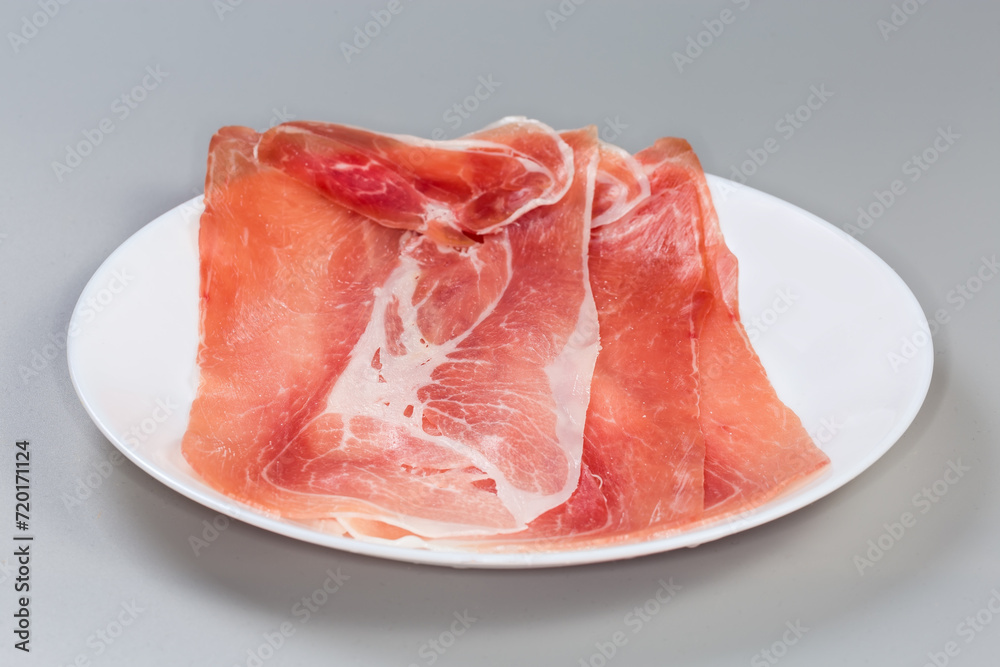 Jamon slices on dish on gray background, side view closeup Jamon slices on dish on gray background, side view closeup