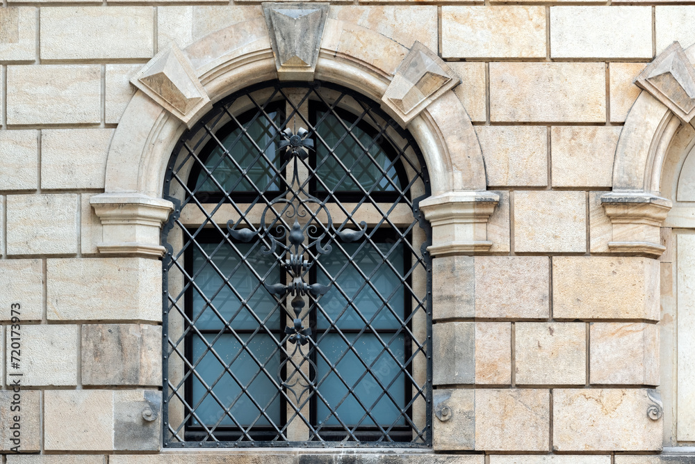 Arched window with wrought metal grille with pattern on the background of a beige colored stone block wall. From the windows of the world series.