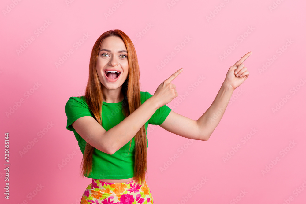 Portrait of overjoyed girl with redhead hair wear stylish top indicating at impressive sale empty space isolated on pink color background Portrait of overjoyed girl with redhead hair wear stylish top indicating at impressive sale empty space isolated on pink color background
