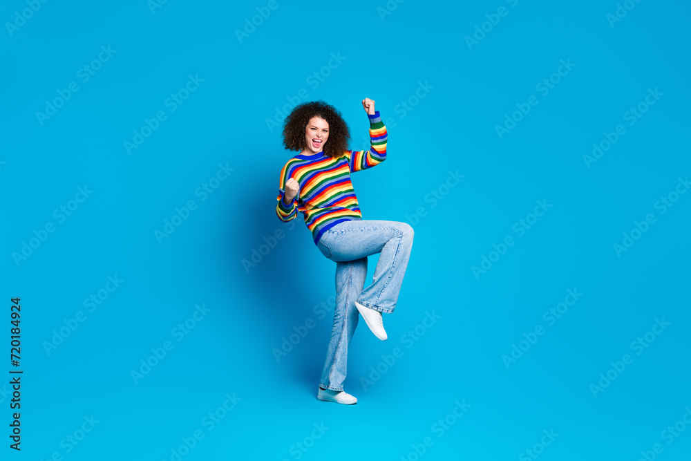 Full body photo of attractive young woman raise fists celebration wear trendy rainbow print clothes isolated on blue color background Full body photo of attractive young woman raise fists celebration wear trendy rainbow print clothes isolated on blue color background