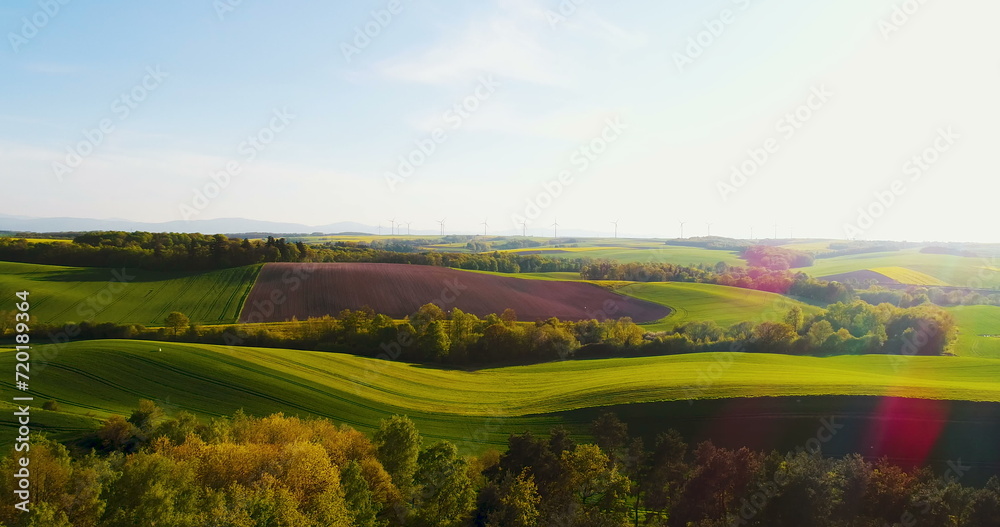 Aerial view of summer countryside with wind turbines and agricultural fields.