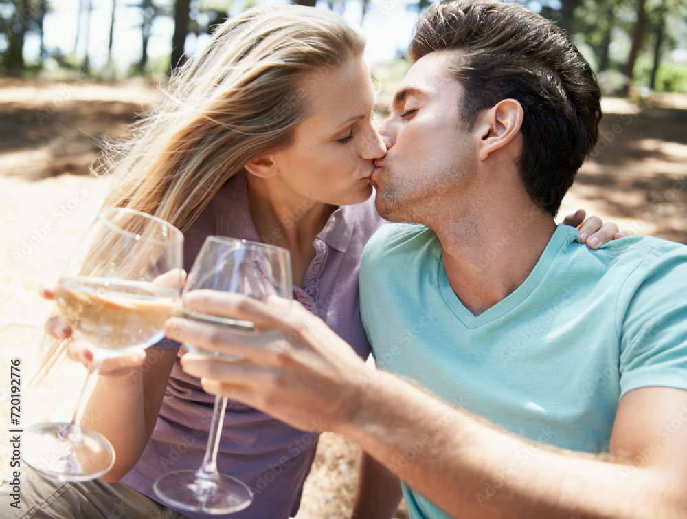 Couple, kiss and wine glass in nature or forest for celebration of love, holiday and valentines day. Man and woman together with alcohol, drinks and toast on outdoor date for anniversary in woods