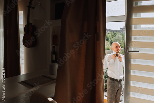 man in shirt dressing up and adjusting tie on neck at home. Wedding day concept,fashion, business, male style. © Vasil