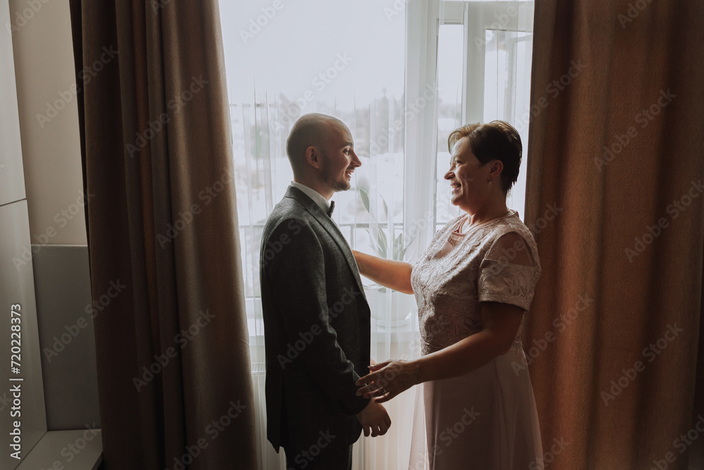 © Vasil - mother helps her adult son prepare for the wedding ceremony. An emotional and touching moment at a wedding. A mother hugs her son © Vasil - mother helps her adult son prepare for the wedding ceremony. An emotional and touching moment at a wedding. A mother hugs her son