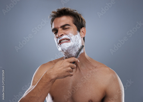 Man, shaving and pain in studio portrait with grooming, skincare and wellness with stress by grey background. Person, model and anxiety with beard, facial hair removal and product for cosmetic change