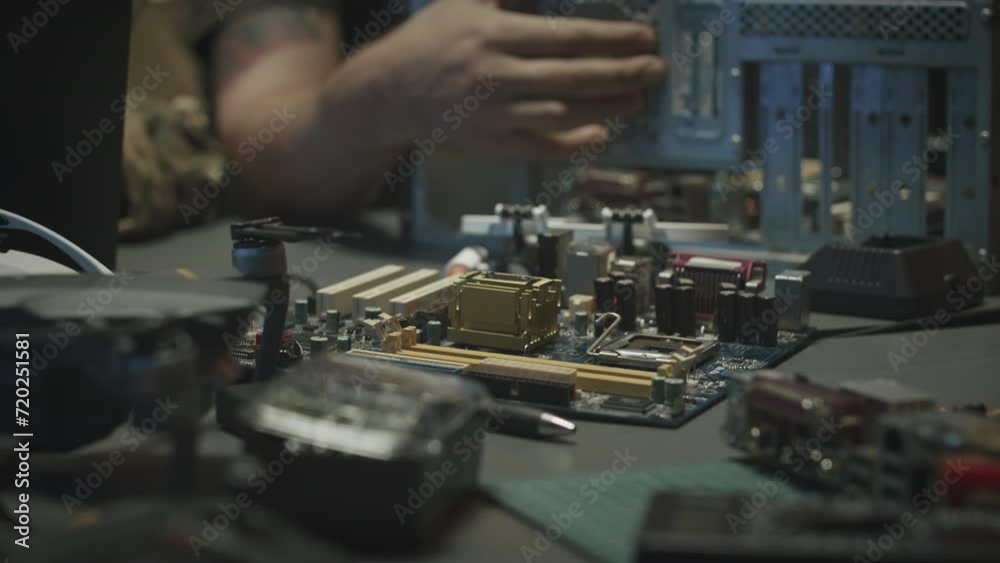 Table with PCBs and surveillance gadgets and devices and unrecognizable military officer assembling computer processor in cyber security center Table with PCBs and surveillance gadgets and devices and unrecognizable military officer assembling computer processor in cyber security center