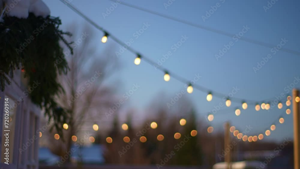 Selective focus shot of outdoor string lights hanging on line on outside house in backyard in cozy evening winter on background of sky. Garden decoration. Party camping. Shooting in slow motion.