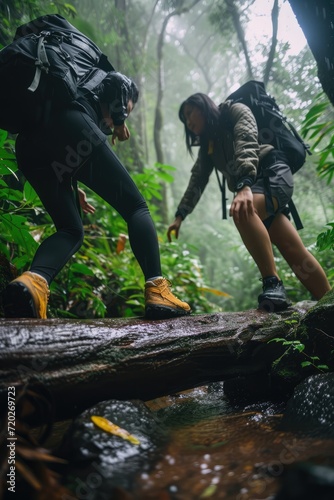 Rainforest Escapade: An Asian Couple Faces the Challenge of Climbing Over a Wet Log in the Dense Jungle Amidst the Rain.