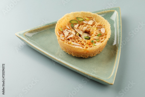 Indian Rajasthani crunchy sweet dish called Ghevar or Ghewar is an made using refined flour, sugar, and ghee. Garnished with silver foil and dry fruits