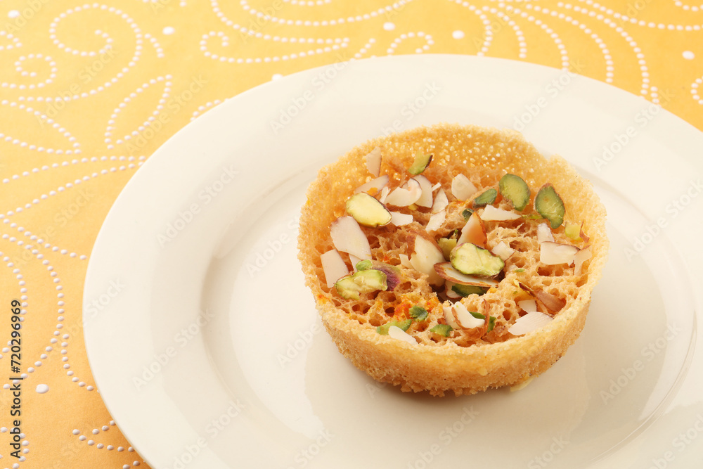 Indian Rajasthani crunchy sweet dish called Ghevar or Ghewar is an made using refined flour, sugar, and ghee. Garnished with silver foil and dry fruits Indian Rajasthani crunchy sweet dish called Ghevar or Ghewar is an made using refined flour, sugar, and ghee. Garnished with silver foil and dry fruits