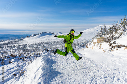 Happy Man jumping Bright acid green outfit: warm suit, goggles, black helmet, gloves, backpack. Snowy mountains background at Sheregesh ski resort. Active lifestyle, winter leisure. Mountain View photo
