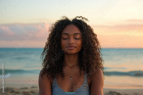 A young black woman with long curly hair doing yoga on the beach