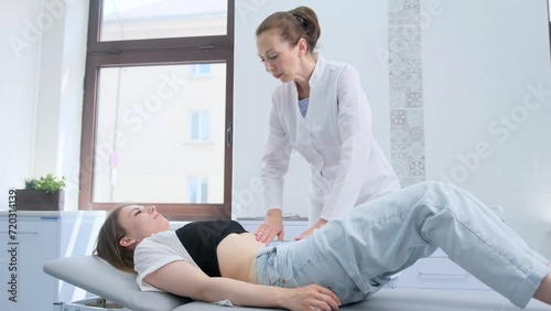 A female doctor feels the stomach of a young female patient lying on a couch Being examined by a gastroenterologist photo