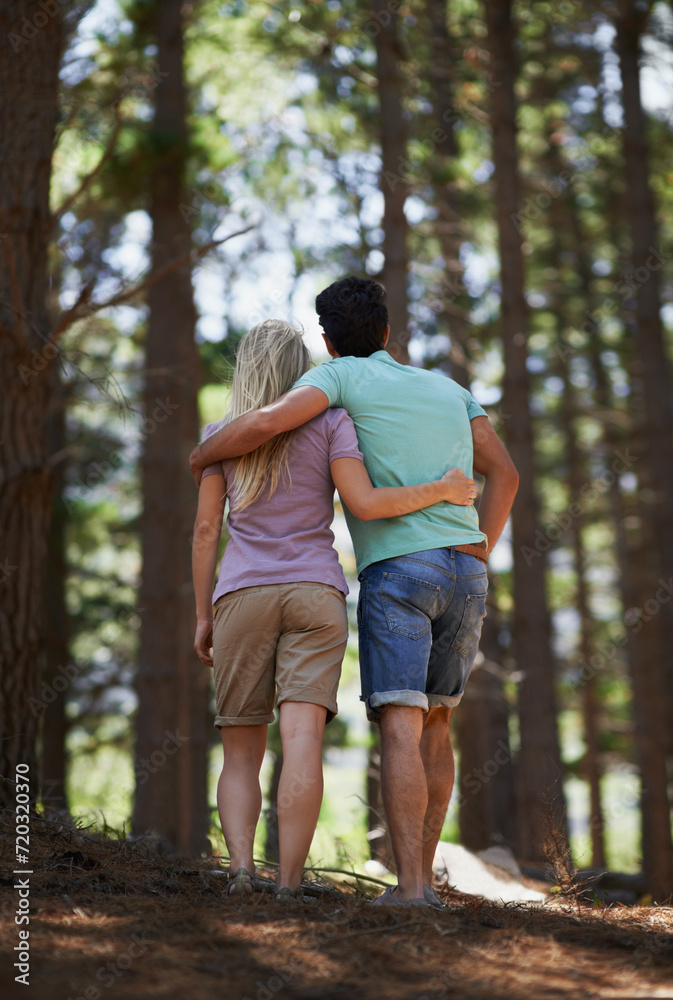 Couple, walking and hug in forest for love, embrace or support in trust, care or bonding in nature. Rear view or back of young man and woman in romance, affection or hiking together in outdoor woods