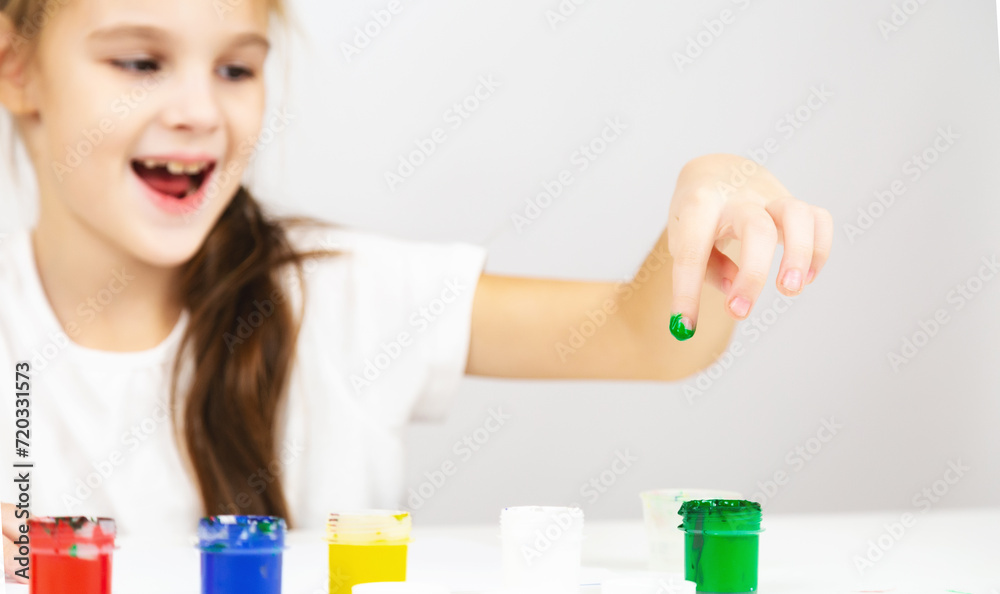 A little girl paints with her fingers at a table indoors. The concept of children's creativity. A little girl paints with her fingers at a table indoors. The concept of children's creativity.