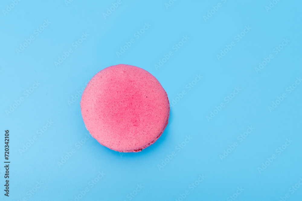 Pink french macaroon or macaron on blue background. Tasty colorful macarons. Cookie made of two smooth halves, fastened with stringy fillings. French pastry made from egg whites. Pink french macaroon or macaron on blue background. Tasty colorful macarons. Cookie made of two smooth halves, fastened with stringy fillings. French pastry made from egg whites.
