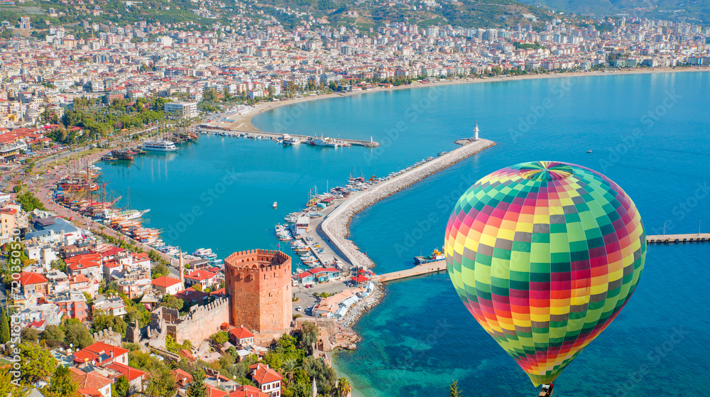 Fototapeta premium Hot air balloon flying over marina and Red Tower (Kizil Kule) in Alanya peninsula - Antalya, Turkey