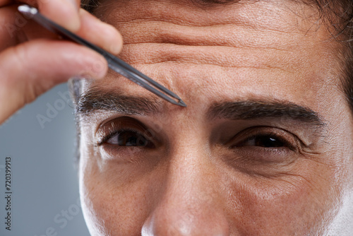 Man, portrait and tweezers for eyebrows in studio or face grooming, hygiene or grey background. Male person, tools and painful hair removal for healthy morning routine or cosmetics, treatment or care