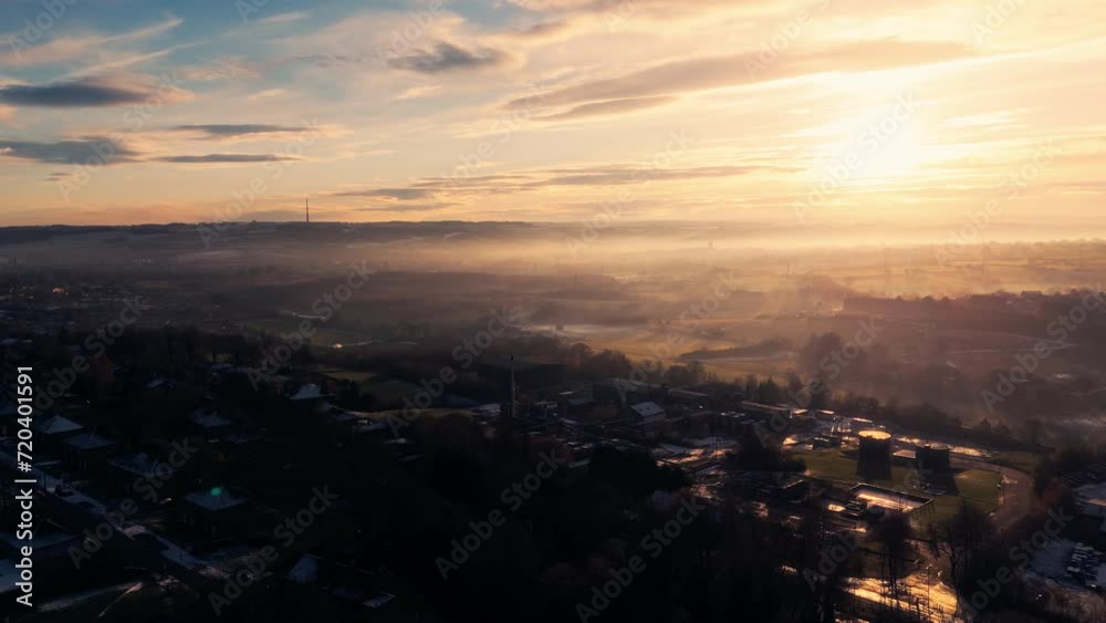 Misty, urban January winters sunset with sun-rays breaking through the mist. Yorkshire aerial scene with red brick houses, industrial buildings, Soft distant mist covering rolling hills and dales. Misty, urban January winters sunset with sun-rays breaking through the mist. Yorkshire aerial scene with red brick houses, industrial buildings, Soft distant mist covering rolling hills and dales.