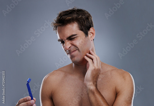 Man, shaving and beard or razor burn in studio for hair removal mistake, inflammation or grey background. Male person, tool and leaning or unhappy accident for wellness maintenance, pain or mockup