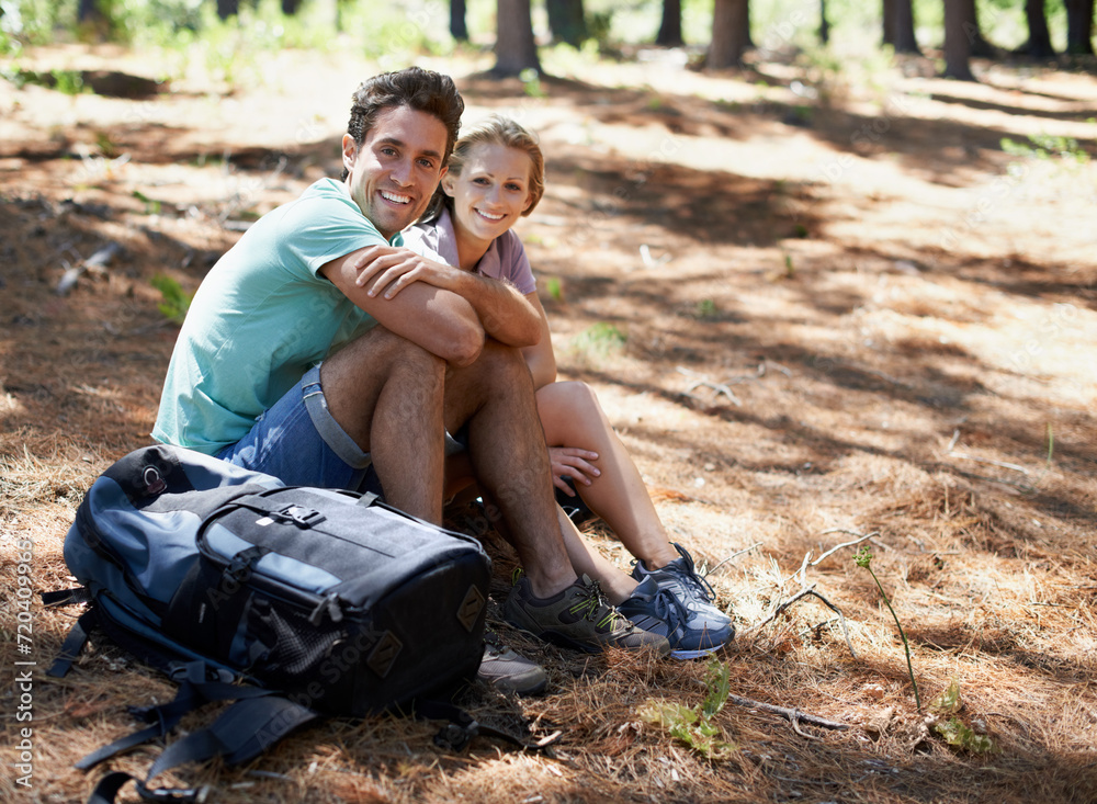Couple, hiking break and portrait in nature for outdoor travel, adventure and wellness journey by forest. Happy man and woman relax on ground with backpack for trekking destination, health or fitness