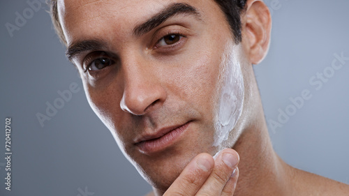 Portrait, cream and man with dermatology, cosmetics and beauty on a grey studio background. Portrait, person and model with grooming routine or skincare with lotion or moisture after shave with shine photo