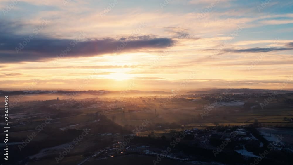 Misty, urban January winters sunset with sun-rays breaking through the mist. Yorkshire aerial scene with red brick houses, industrial buildings, Soft distant mist covering rolling hills and dales. Misty, urban January winters sunset with sun-rays breaking through the mist. Yorkshire aerial scene with red brick houses, industrial buildings, Soft distant mist covering rolling hills and dales.