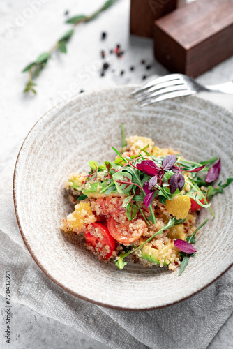 Fresh salad with quinoa, avocado, tomatoes, herbs and vegetables in a gray ceramic bowl on a concrete background. Dietary healthy dish for vegans, selective focus