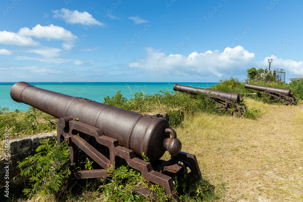 A row of three ancient cannons pointed toward the harbor at Fort James on the island of Antigua in the Caribbean.