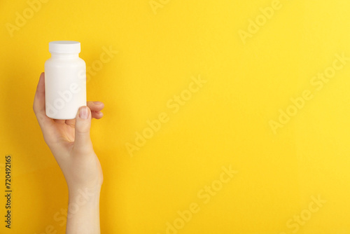 Woman holding blank white jar of vitamins on yellow background, closeup. Space for text