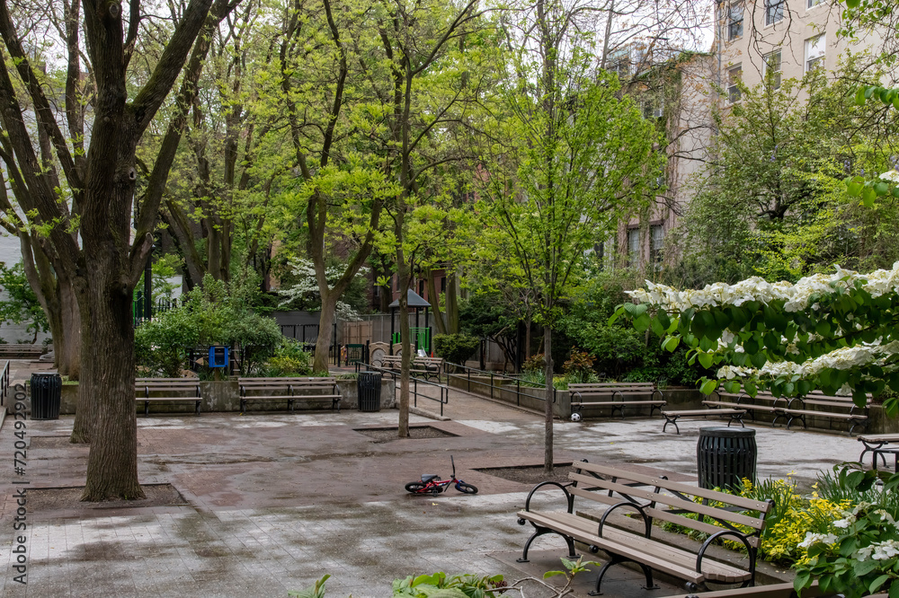 New York City, NY, USA; View over a typical neighborhood playground in Manhatten with equipment and surrounded by trees and park benches; one small kids bike deserted in 