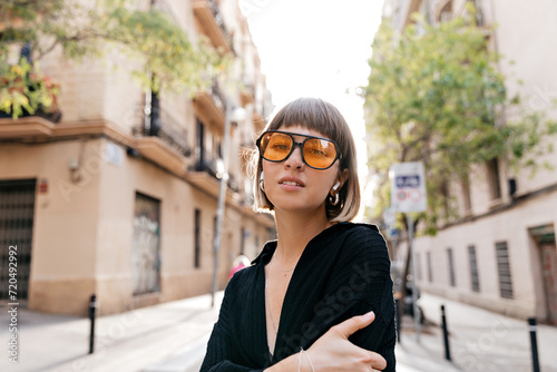 Stylish modern woman with short hair wearing modern glasses posing to camera in sunlight 