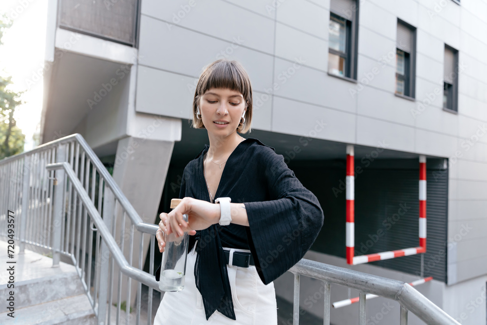 © PhotoBook - Excited stylish fairly with short hair is checking her smart watch on modern city building