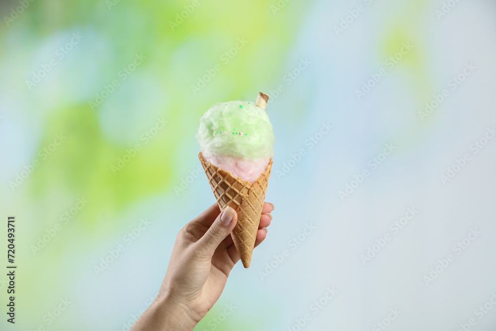Woman holding waffle cone with cotton candy on blurred background, closeup