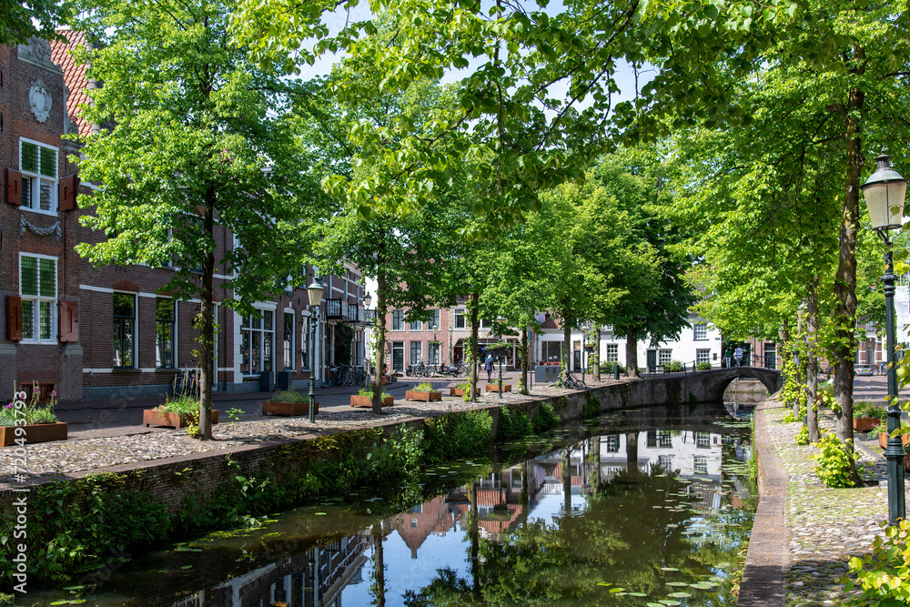 Amersfoort, the Netherlands; View of bridge and street on Havik canal with historic buildings and green trees reflected in the tranquil water of the canal 