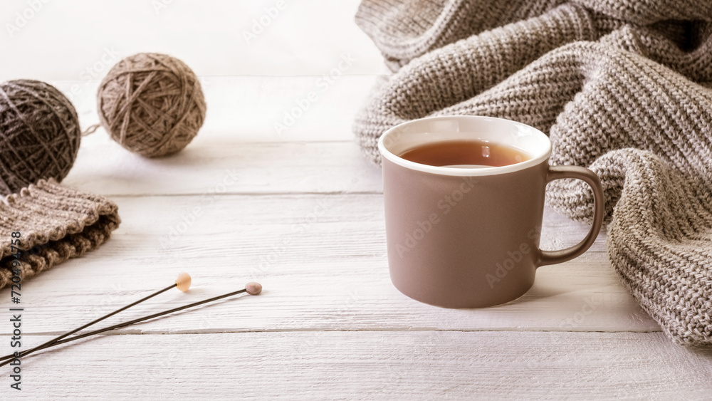 Warm and cozy: a cup of tea surrounded by knitted items and wool yarn balls