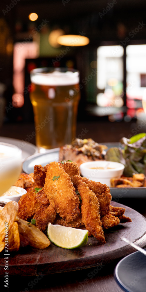 Portion of fried fish fillets on bar table appetizer with beer and blurred background