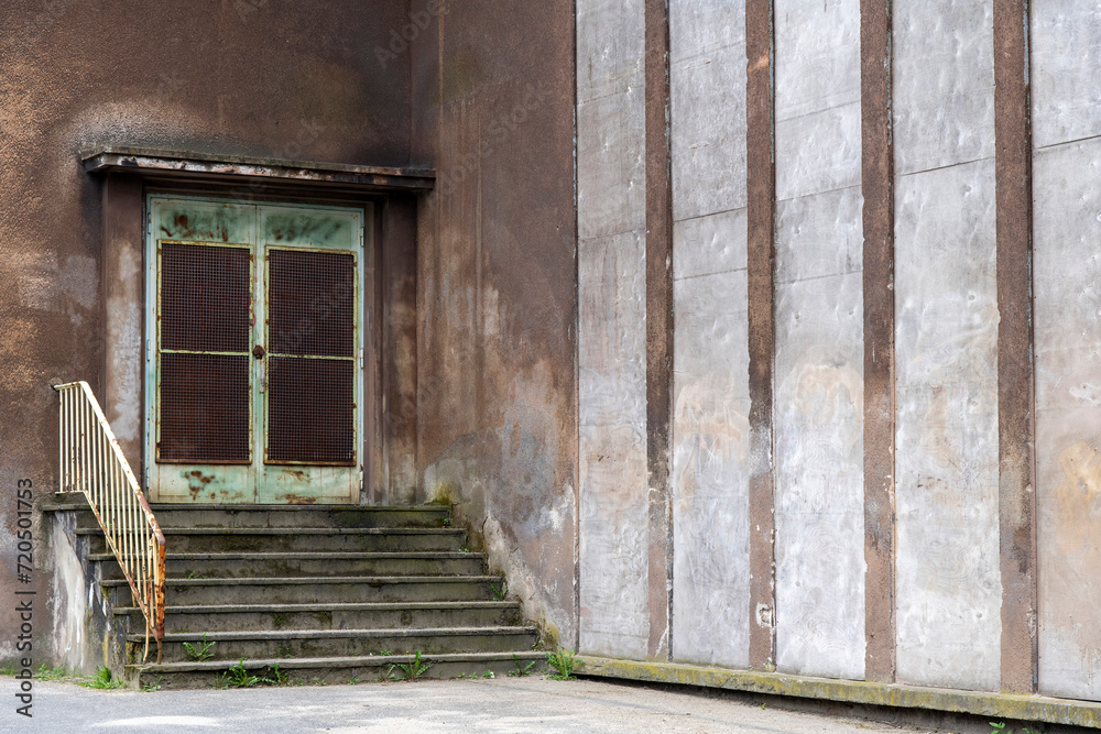 Close up of stairs with rusty entrance door of building of an abandoned and dilapidated industrial steel mill in public Landschaftspark, Duisburg, Germany with striped pattern concrete on facade