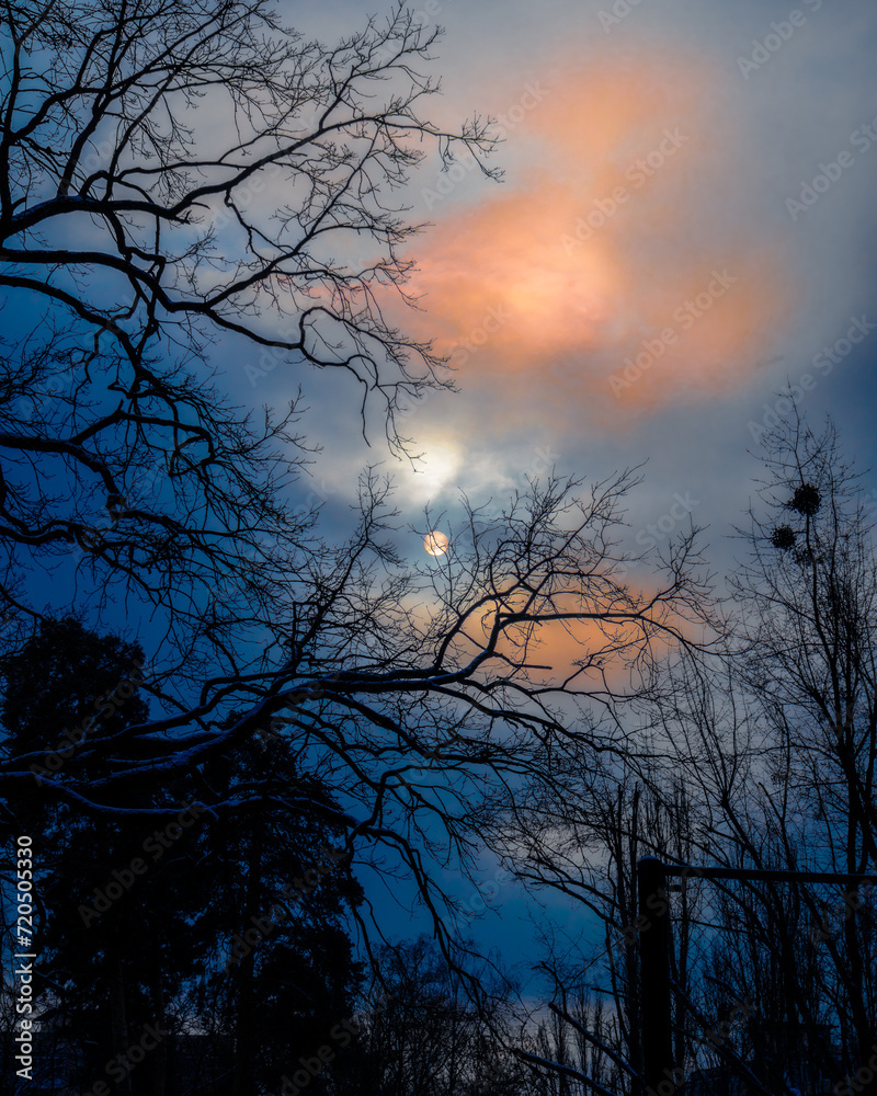 The clear outline of the sun behind blue-orange clouds. Dim sun on a cloudy day The clear outline of the sun behind blue-orange clouds. Dim sun on a cloudy day