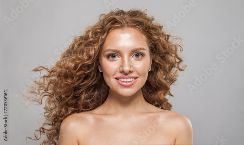 Young redhead female model with long frizzy ginger hair and clean soft fresh skin posing on white background. Studio fashion beauty portrait of young woman