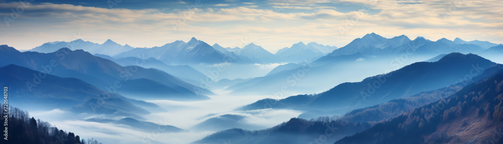 Panoramic view of a majestic mountain range enveloped in morning mist under soft dawn sky.