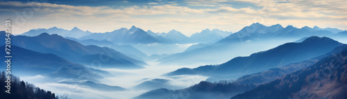 Panoramic view of a majestic mountain range enveloped in morning mist under soft dawn sky. © LunaLu