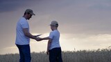 Happy family, child father walk together on wheat plantation in summer. Farmer father works with digital tablet in wheat field with his son. Handshake between father, son. Family business, farmers
