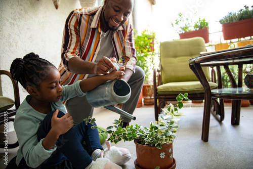 Father and daughter watering a plant at home together photo
