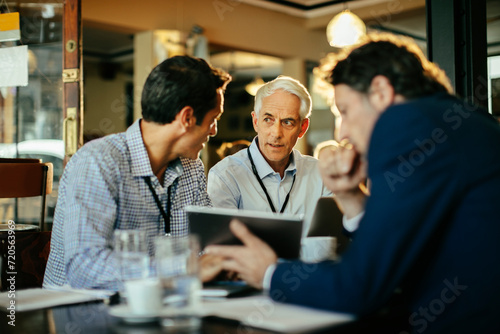 Business meeting in a cafe with three men discussing over a tablet photo