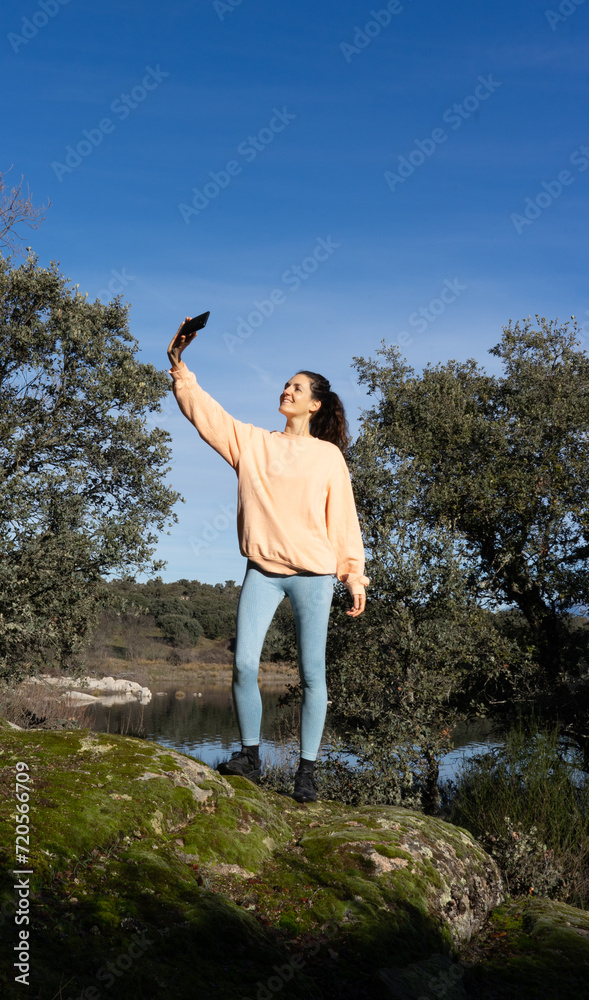 Woman taking a selfie with her cell phone in nature dressed in peach color Woman taking a selfie with her cell phone in nature dressed in peach color