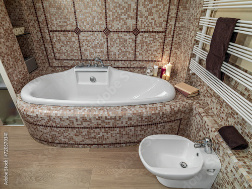 interior view of a modern bathroom, in foreground the bidet in background the bathtub, the walls are coated with mosaic tiles instead the floor is mae of wood (ID: 720570341)