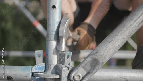 A man hammers a wedge pin into metal scaffolding. Close-up of scaffolding installation.