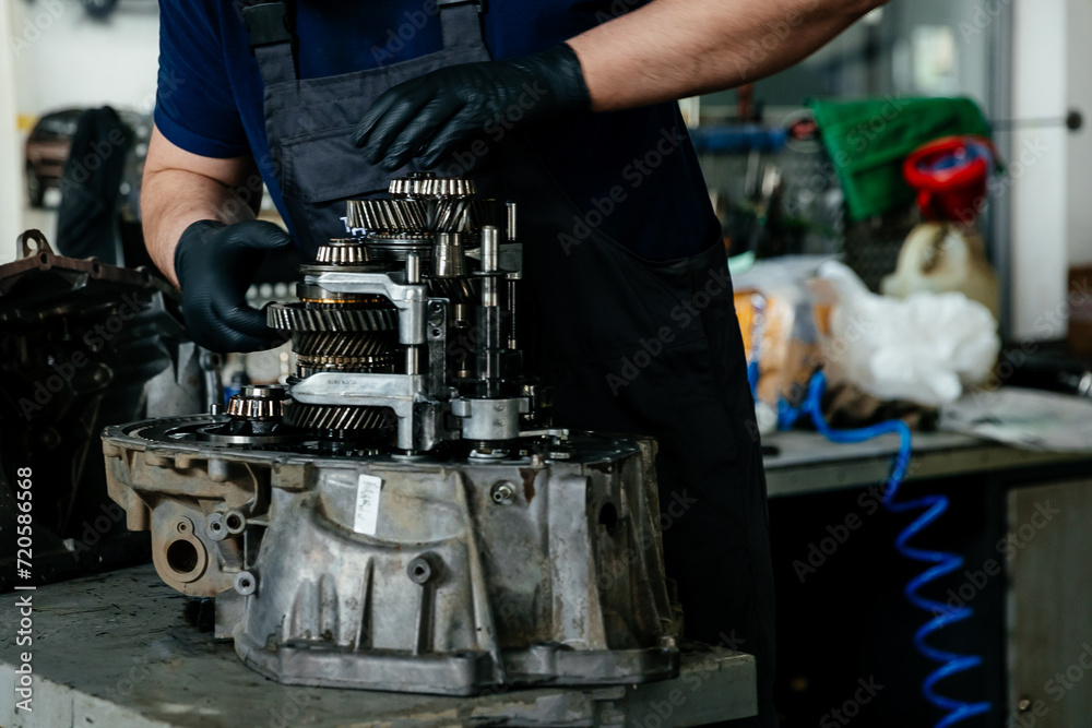 a disassembled gearbox in the hands of an experienced car mechanic who repairs broken mechanisms and parts in a car - obrazy, fototapety, plakaty 